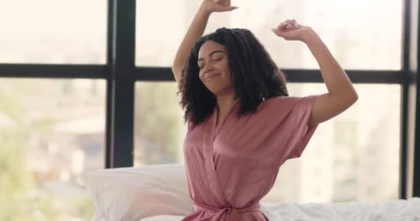 Laiska aamu. Nuori hyvin nukkunut afrikkalainen amerikkalainen nainen pyjamassa venyttely, istuu sängyssä, herääminen - Materiaali, video