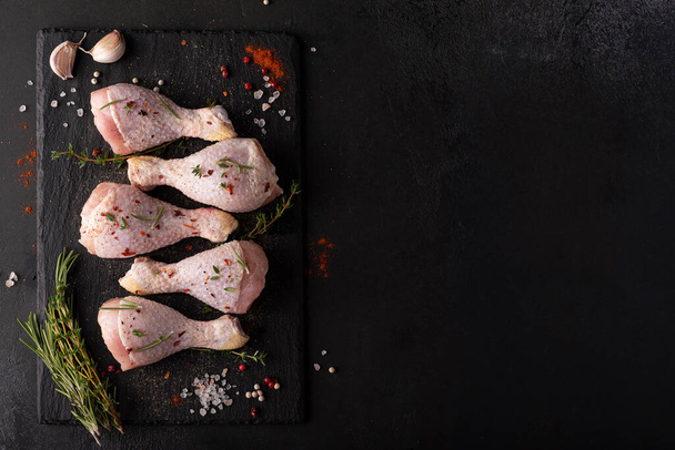 raw chicken drumsticks with spices and herbs on black board, top view - Foto, Bild