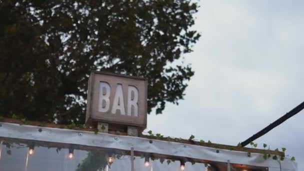 Panneau de bar en bois au-dessus d'une pergola couverte éclairée avec un arbre derrière elle - Séquence, vidéo
