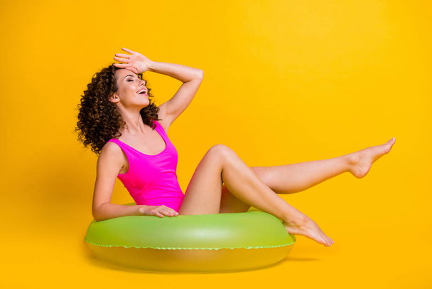 Photo portrait of laughing brunette girl sunbathing sitting in green inflatable ring isolated on vivid yellow colored background - Photo, Image