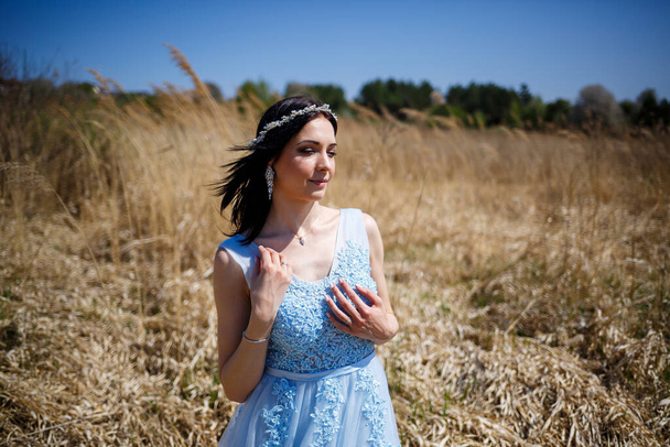 Портрет ніжної дівчини в блакитній довгій сукні в сухому горошку з посмішкою на обличчі в сонячний теплий літній день
 - Фото, зображення