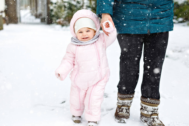 母親と一緒に冬に屋外で最初の一歩を踏み出す愛らしい小さな赤ちゃんの女の子。かわいい幼児歩くことを学ぶ. - 写真・画像