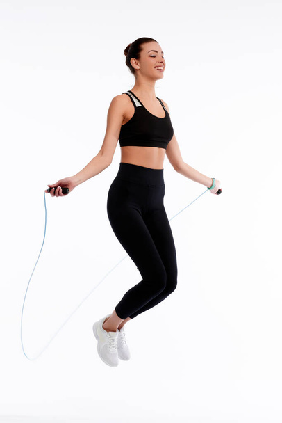 Spotrswoman jumping with rope on white isolate background. Fitness female doing physical exercise. Healthcare and weightlose concept - Фото, изображение