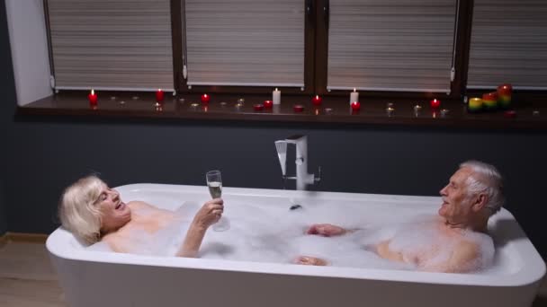 Starší pár zamilovaný ležící v teplé koupeli s bublinkami, užívající si relaxaci, popíjení šampaňského - Záběry, video