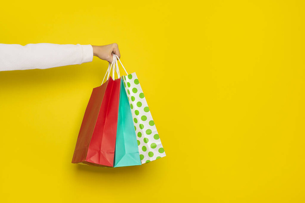 Concepto de compra o venta. La mano femenina sostiene bolsas de papel aisladas sobre fondo amarillo. Banner con espacio de copia - Foto, Imagen