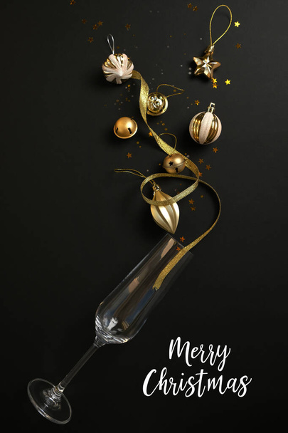 Wine glasses with golden confetti and stars and gold christmas decorations with the inscription Merry Christmas on black background. Flat lay, top view. Holiday and celebration concept. - Photo, image