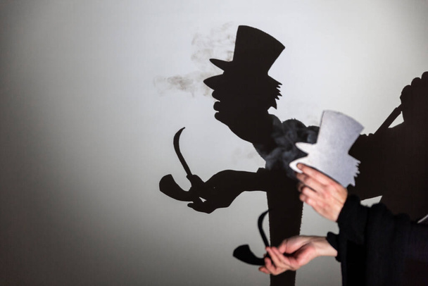 play shadow projected on a white screen. the person's hands shape a gentleman wearing a hat, scarf and smoking a pipe. - Photo, Image