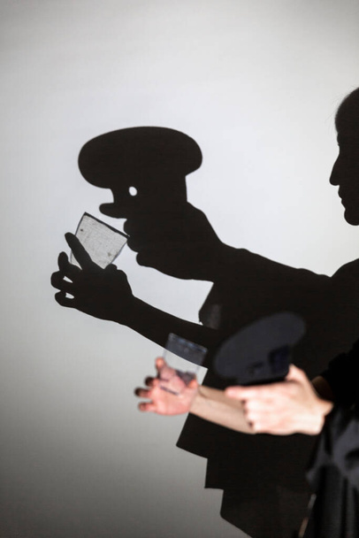 jogar sombra projetada em uma tela branca. as mãos da pessoa moldam um cozinheiro bebendo de um copo - Foto, Imagem