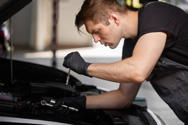 young caucasian auto mechanic in a car service, checks a car, engine, carburetor - Foto, Bild