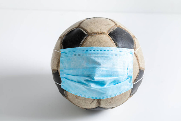 Coronavirus and soccer concept. Old Football ball in medical mask on white background - Фото, изображение