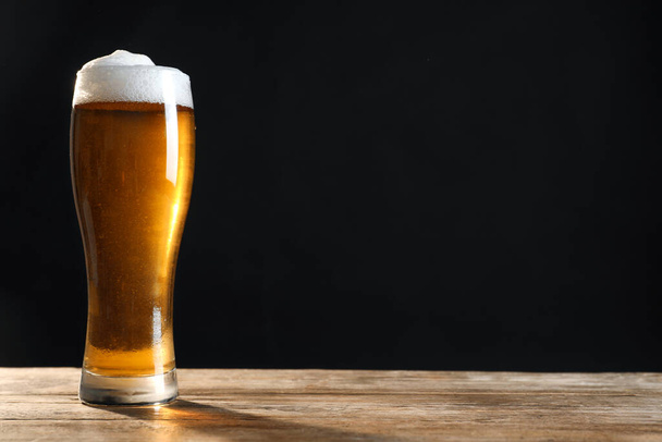 Cold tasty beer on wooden table against dark background. Space for text - 写真・画像