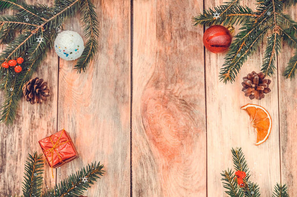 Christmas frame made of fir branches, red Rowan berries, red gift box, pine cones, Christmas balls, dried orange slices on a wooden background. Top view copy space. Beautiful Christmas background - Photo, image