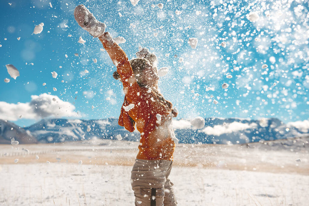 Adult girl throws snow and having fun against mountains - Foto, afbeelding