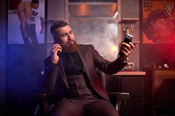 elegant barber male hold electric razor in hands and talk on phone - 写真・画像