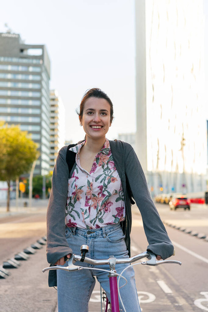vertical portrait of a smiling young woman at the city riding a pink retro bicycle by the bike path, concept of active lifestyle and sustainable mobility - Foto, Bild