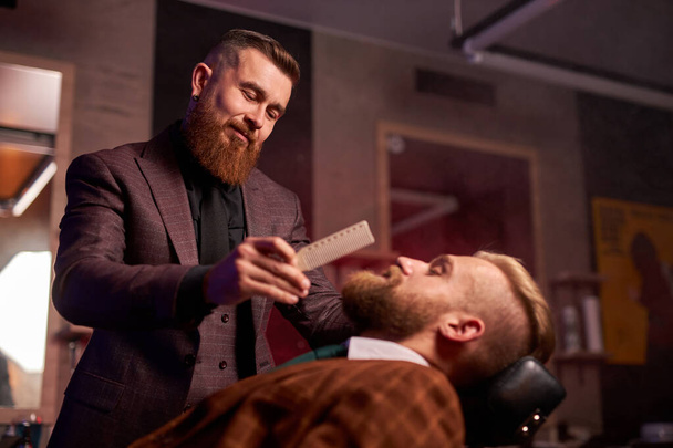 hairstyling process. barber cutting beard of caucasian male - Foto, afbeelding