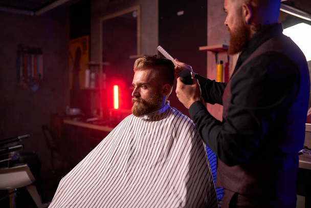 confident male hairstylist cut hair to elegant stylish man sitting in salon - Fotó, kép