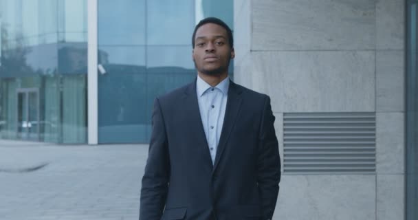 Magabiztos afro-amerikai üzletember öltönyben sétál a modern irodaház közelében, lassított felvétel - Felvétel, videó