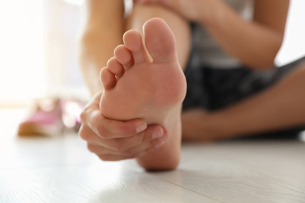 Young woman suffering from pain in foot on floor, closeup - Φωτογραφία, εικόνα
