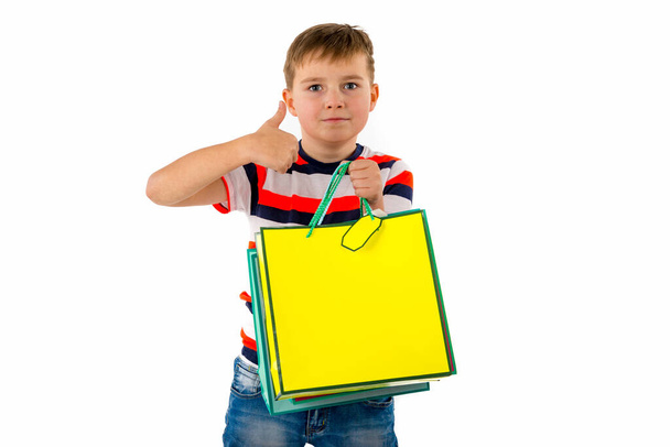 Szekrény Fiatal fiú, kezében bevásárló színes táskák mutatja hüvelykujj up Holiday Eladó. fehér háttér. - Fotó, kép