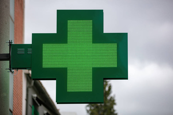 Simbolo del segno della farmacia. Croce verde al neon appesa fuori dalla farmacia contro il cielo nuvoloso in città - Foto, immagini