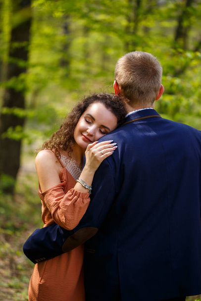 Um belo casal na floresta. Menina com corte de cabelo elegante abraça seu homem em um terno. Rústico ao ar livre detalhes retrato de fotografia. Mulher feliz e namorado - Foto, Imagem