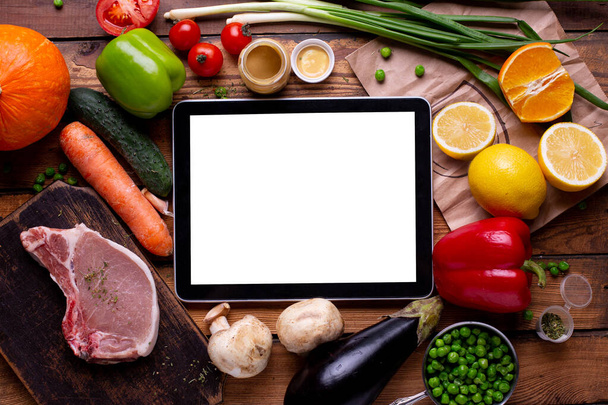 Electronic tablet white empty screen temperate with meat and different vegetables on a wooden background top view - Foto, immagini