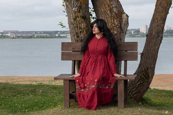 beautiful young girl in a red boho dress with long sleeves walks in the park - Valokuva, kuva