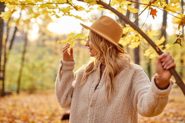 side view on blonde female in hat posing in autumn forest - Foto, Imagen