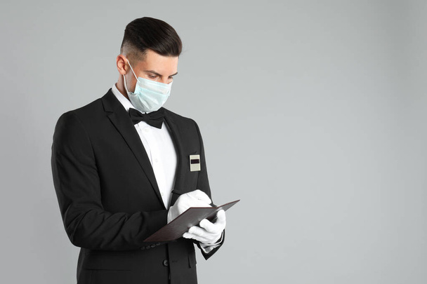 Waiter in medical face mask taking order on light grey background. Space for text - Foto, imagen