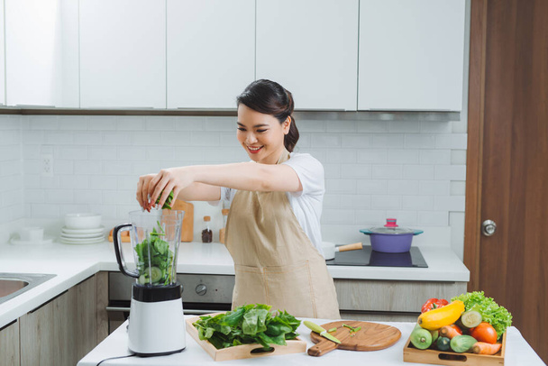 Mutfaktaki blender eviyle yeşil smoothie karıştıran sebzeli kadın. - Fotoğraf, Görsel