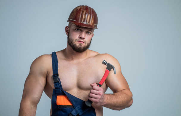 athletic guy with strong muscles in mechanic uniform with hammer, carpenter - Φωτογραφία, εικόνα