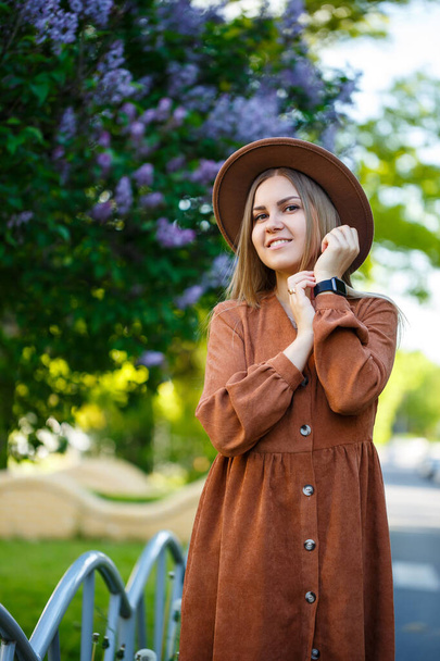 Красивая длинноволосая девушка в шляпе на фоне сиреневых цветов - Фото, изображение