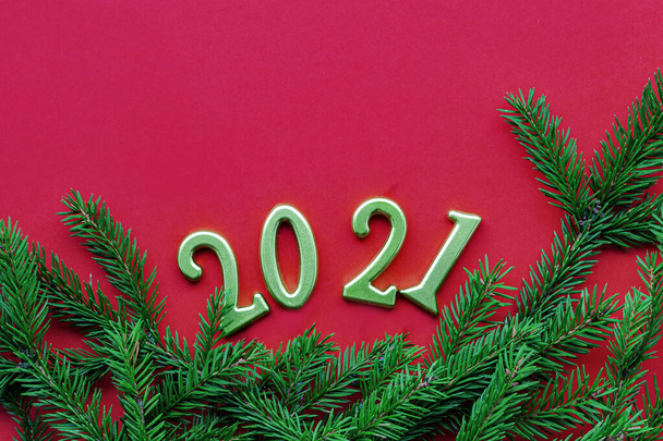 Numeri d'oro 2021 e verde albero di Natale ramo solido sfondo rosso. Capodanno e Natale concetto di vacanza. Posa piatta, spazio di copia. - Foto, immagini