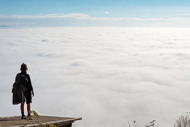 Mujer de pie sobre una plataforma de madera y disfrutando de la vista del valle cubierto de niebla por debajo. Senderismo, logros, expectativas, optimismo y conceptos de autorreflexión. - Foto, Imagen