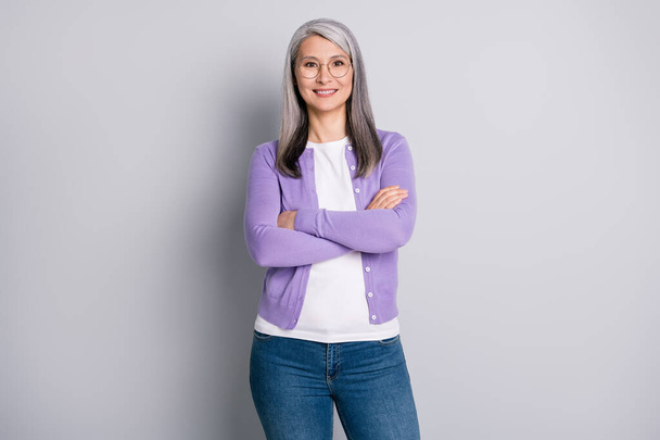 Photo of charming pretty old lady crossed hands self-assured toothy beaming smile wear white shirt purple cardigan glasses denim jeans isolated grey color background - Fotoğraf, Görsel