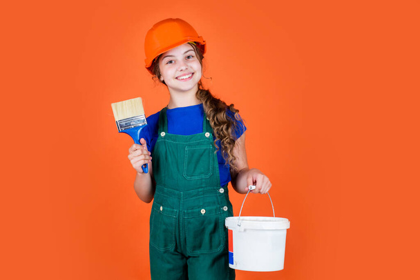 Working in repair shop. kid wear helmet on construction site. teen girl painter with painting bucket and brush. child on repairing work. concept of renovation in workshop. busy professional carpenter - Foto, Imagem