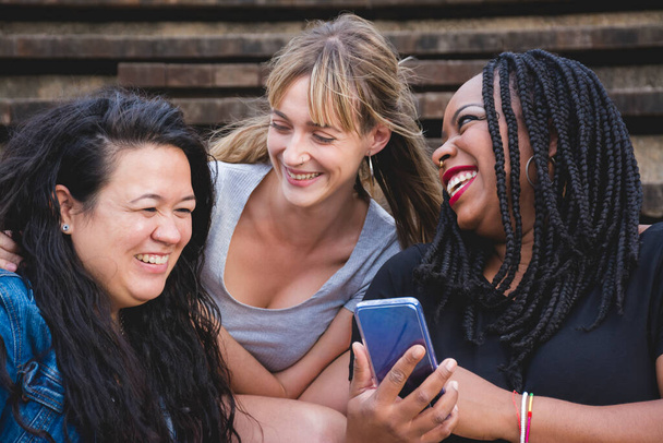 Ryhmä hymyileviä nuoria naisia eri rotuja jakaa hauskoja hetkiä älypuhelimella. Käsitteet kuten monimuotoisuus, ystävyys, kumppanuus - Valokuva, kuva