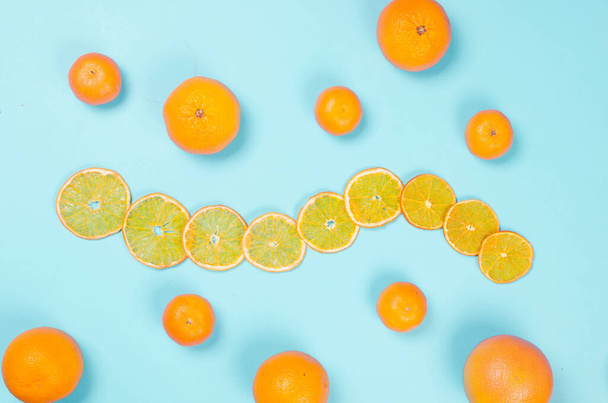 Ripe juicy oranges and tangerines with dried orange chips scattered on blue background. Fruit chips. Healthy eating concept, snack, no sugar. Top view, copy space.  - Foto, imagen