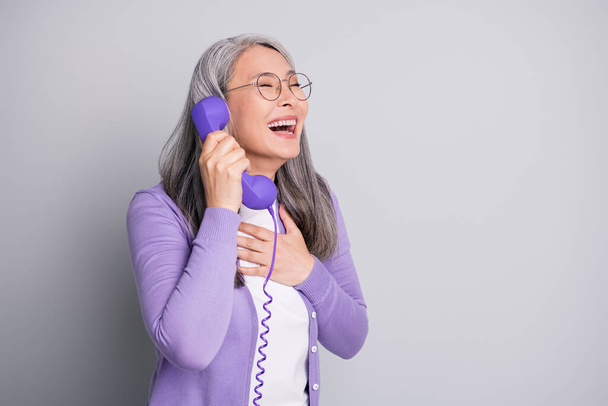 Photo portrait of elder funny laughing woman smiling talking on old retro purple phone with wire isolated on grey color background - Photo, Image