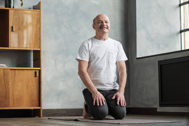 Homem sênior praticando ioga em casa sentado em Vajrasana pose. - Foto, Imagem