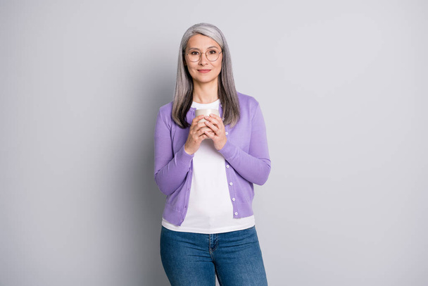 Photo portrait of woman holding cup with two hands wearing violet shirt isolated on grey colroed background - Fotoğraf, Görsel