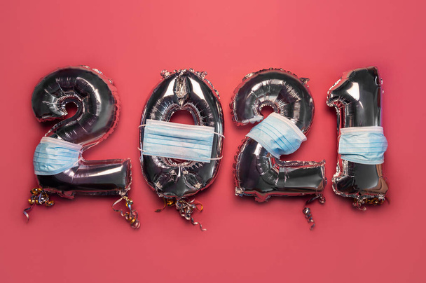 Ballon Bunting zur Feier des neuen Jahres 2021 aus silbernen Zahlenballons mit schützenden Gesichtsmasken auf rosa Hintergrund. Feiertagsdekoration oder Postkartenkonzept als neue Realität - Foto, Bild