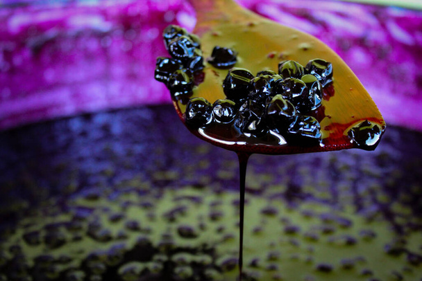 Grupa jagód aronii na drewnianej łyżce do gotowania, ciekły dżem wycieka i kapie z łyżki do garnka z dżemem dławikowym. Zavidovici, Bośnia i Hercegowina. - Zdjęcie, obraz