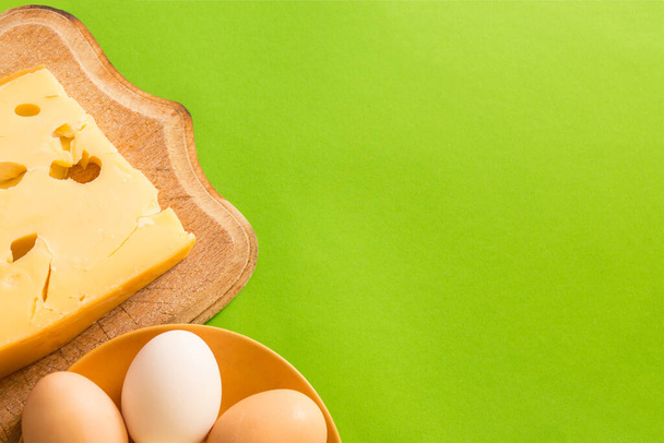 Tabakta yumurta ve yeşil arka planda fotokopi alanı olan bir tahtanın üzerindeki Maasdam peyniri.. - Fotoğraf, Görsel