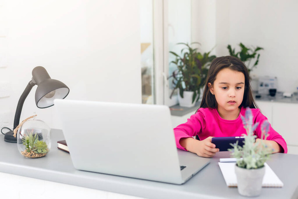 Etäopetus. Lapsi hymyilee iloisesti ja saa tietoa etänä. Pikkutyttö opiskella verkossa oppimista kotoa kannettavan. Online koulu. - Valokuva, kuva