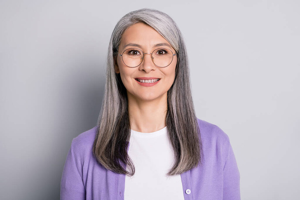 Portrait photo of positive smiling elder woman wearing eyeglasses and purple cardigan isolated on grey color background - Foto, immagini