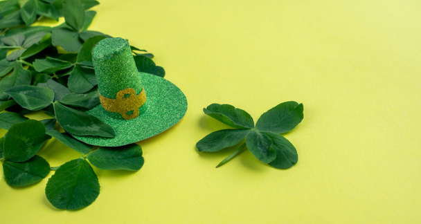 Ένα σύμβολο του καπέλου του Αγίου Πατρικίου, ξωτικό, τριφύλλι. Χαρούμενο τριφύλλι. Πράσινα τριφύλλια απομονωμένα σε κίτρινο φόντο. - Φωτογραφία, εικόνα