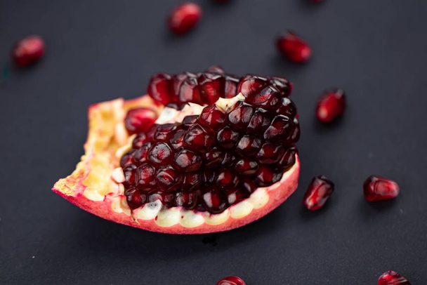fresh ripe pomegranate on a black background. the cut of the pomegranate and its seeds are scattered. Macro photography - Фото, зображення