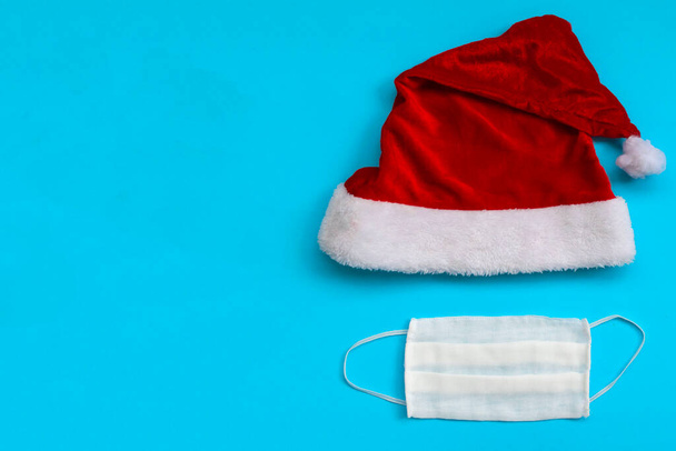 Santa Claus hat and medical mask on light blue background. Christmas and New Year concept. flat lay with space for text - Fotó, kép